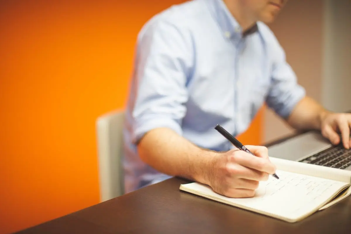 Focus Photography of Person Writing on Desk Using Laptop 1.00