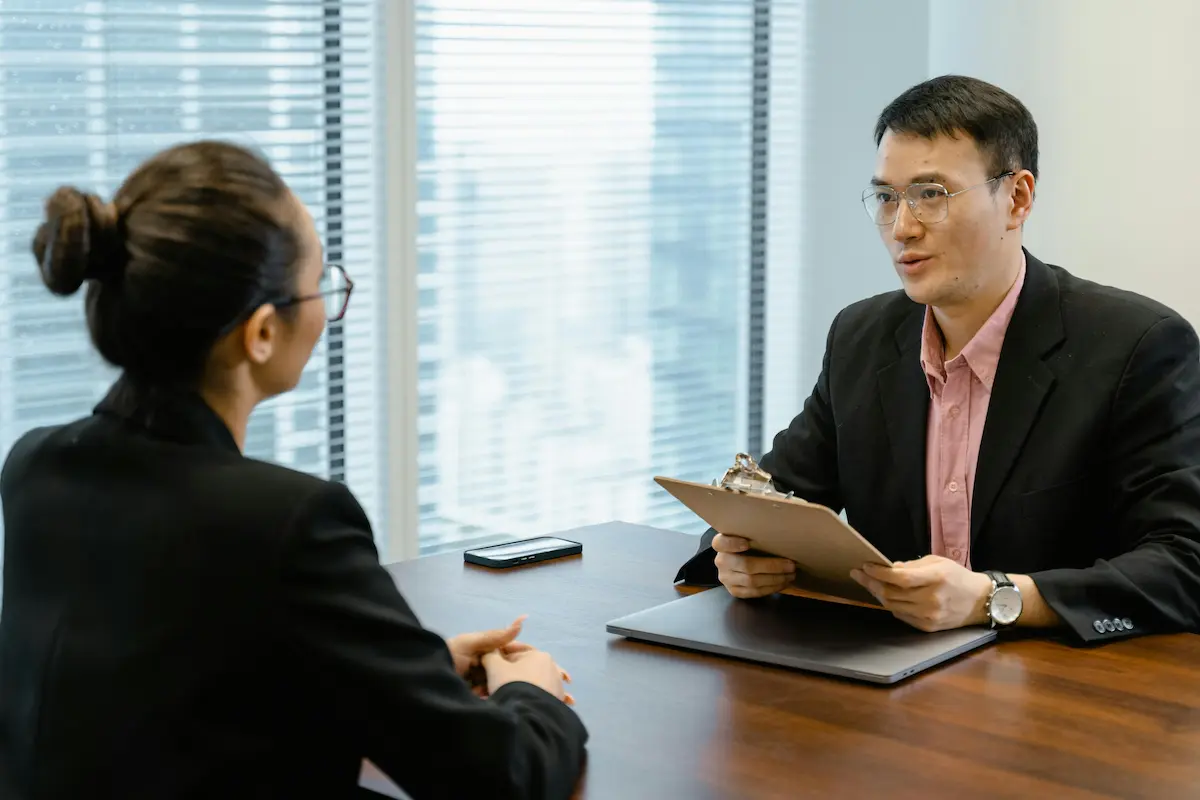 Two professionals discussing at an office table, indicating a formal meeting setting. Two professionals discussing at an office table, indicating a formal meeting setting.
