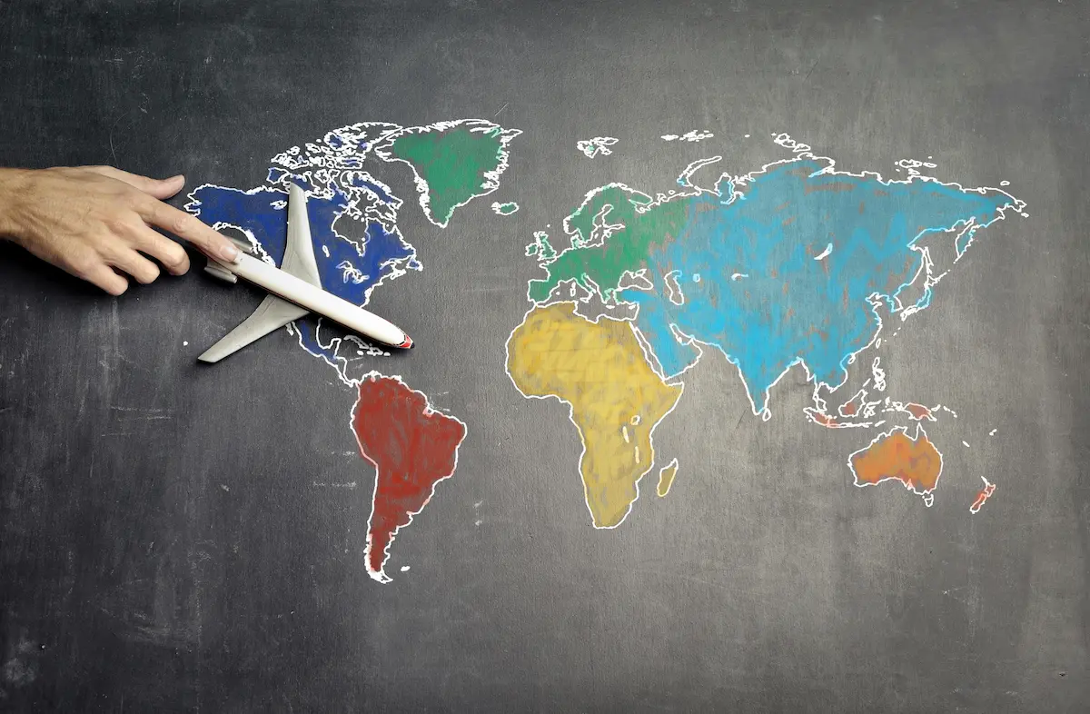 A hand guides a toy airplane over a colorful world map drawn on a chalkboard, symbolizing travel and exploration. A hand guides a toy airplane over a colorful world map drawn on a chalkboard, symbolizing travel and exploration.