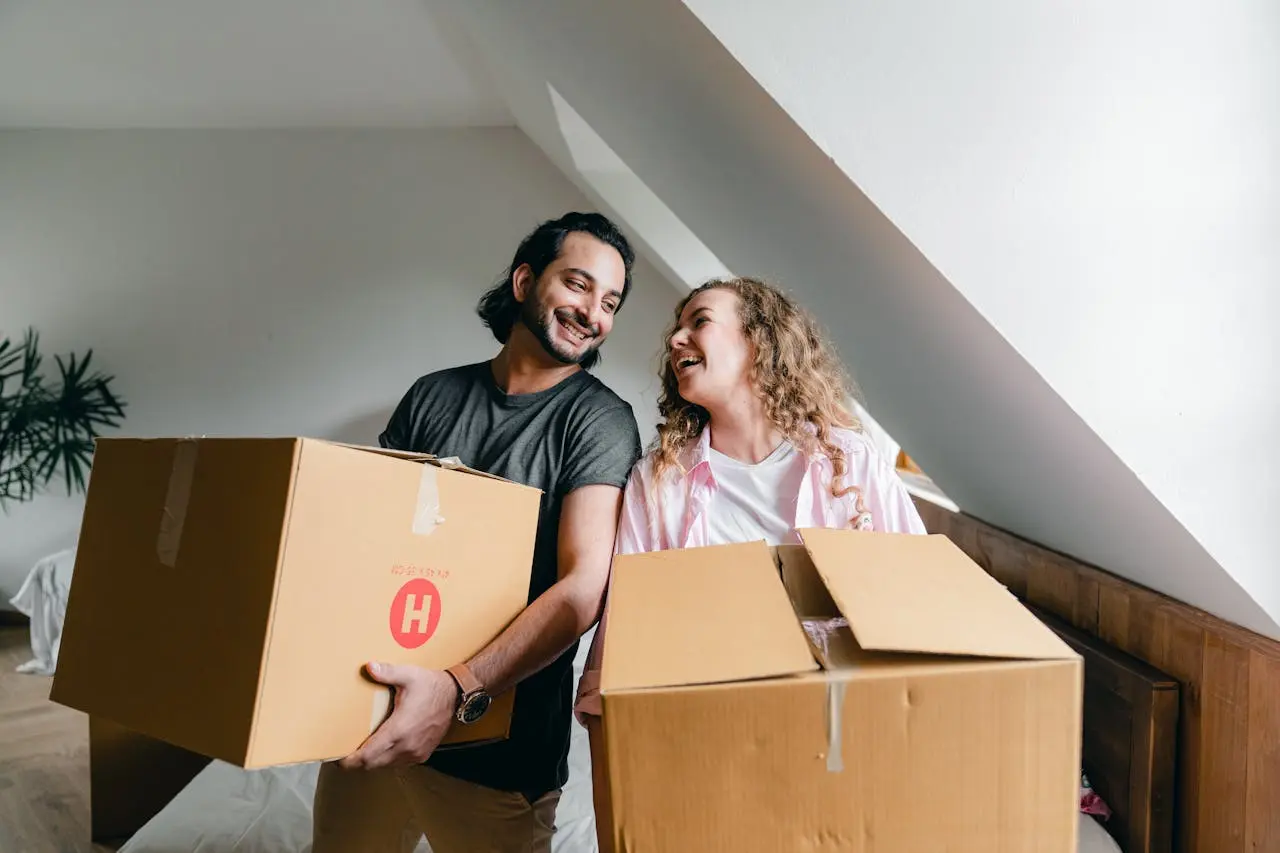 A cheerful couple carrying boxes while moving into their new apartment, sharing a joyful moment indoors. A cheerful couple carrying boxes while moving into their new apartment, sharing a joyful moment indoors.