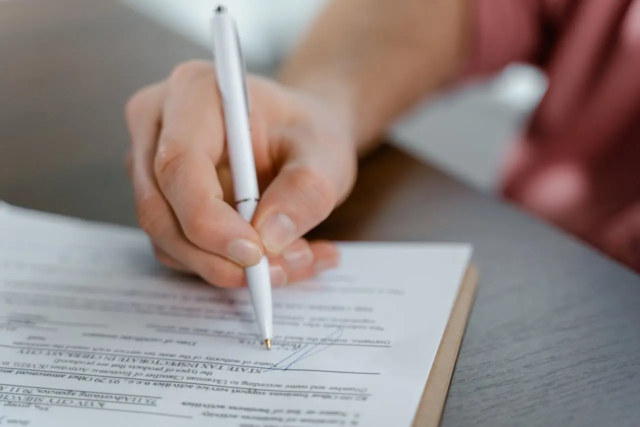 Detailed view of a hand writing a signature on an official document with a ballpoint pen. Detailed view of a hand writing a signature on an official document with a ballpoint pen.