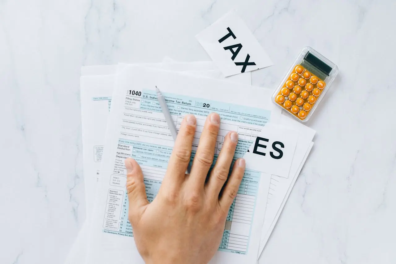 Close-up of a hand on tax form with a calculator on a desk. Close-up of a hand on tax form with a calculator on a desk.