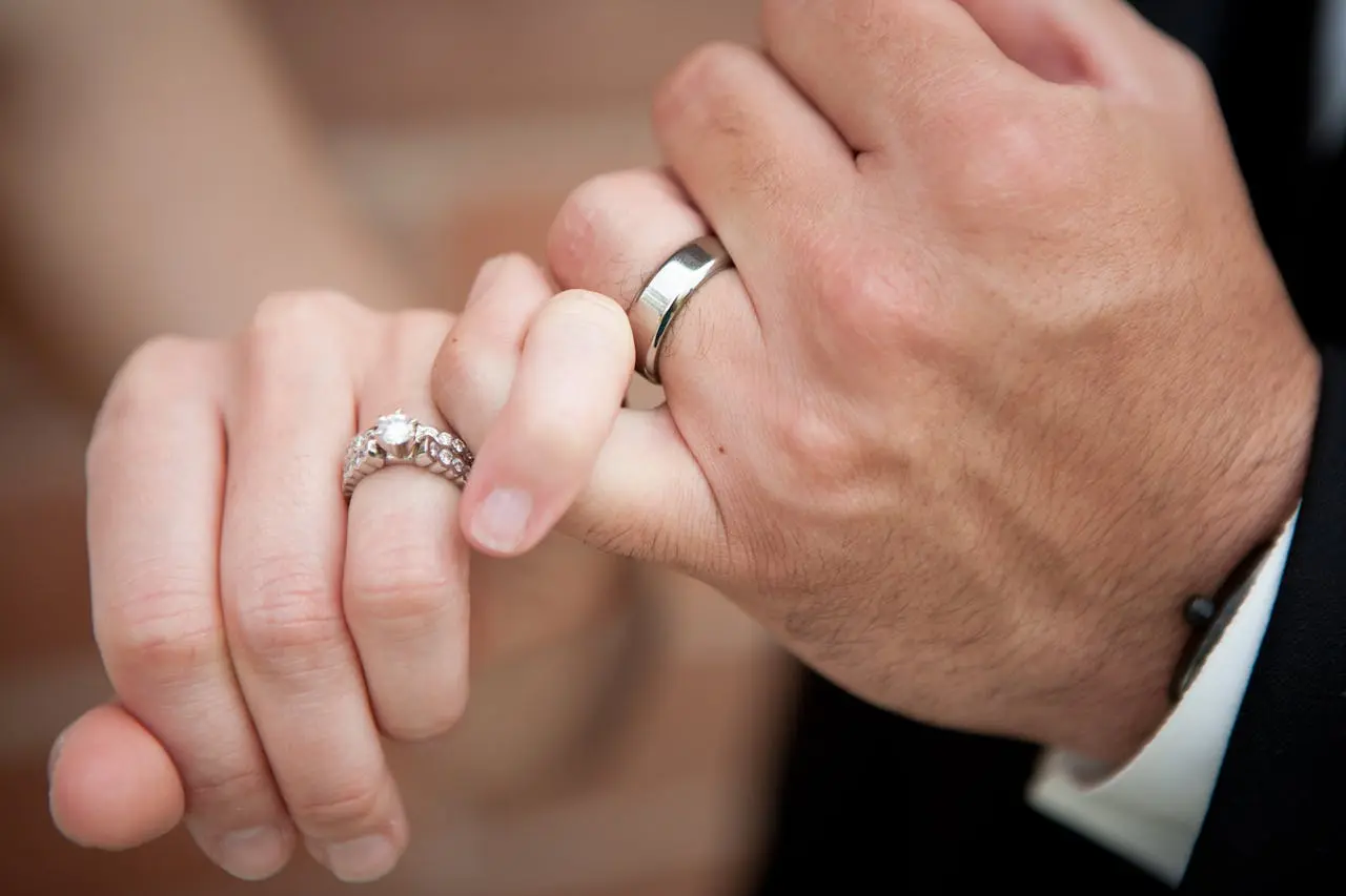 A close-up photo of a couple&rsquo;s hands interlocked, wearing wedding and engagement rings.