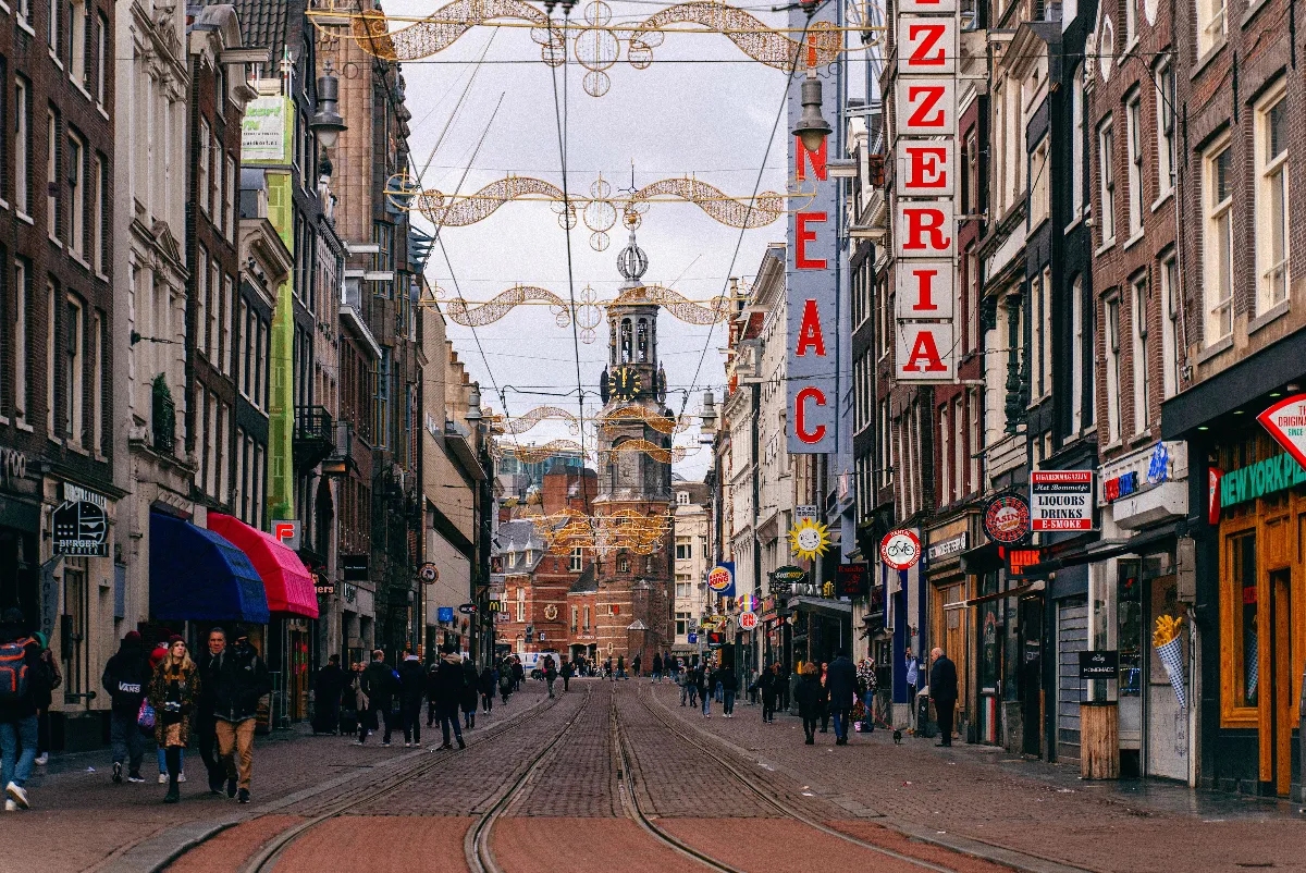 A lively street scene in Amsterdam featuring historic buildings, a clock tower, and pedestrians. A lively street scene in Amsterdam featuring historic buildings, a clock tower, and pedestrians.