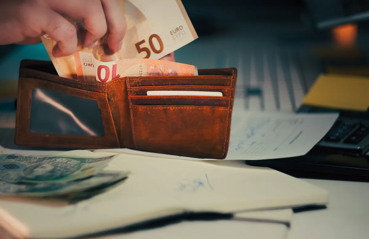 A wallet with euro banknotes and documents on an office desk, symbolizing finance and budgeting. A wallet with euro banknotes and documents on an office desk, symbolizing finance and budgeting.