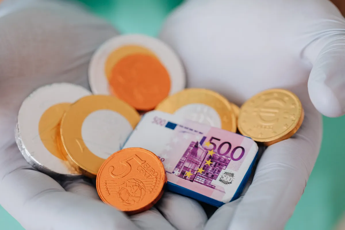 A gloved hand displaying chocolate coins and a euro banknote. A gloved hand displaying chocolate coins and a euro banknote.