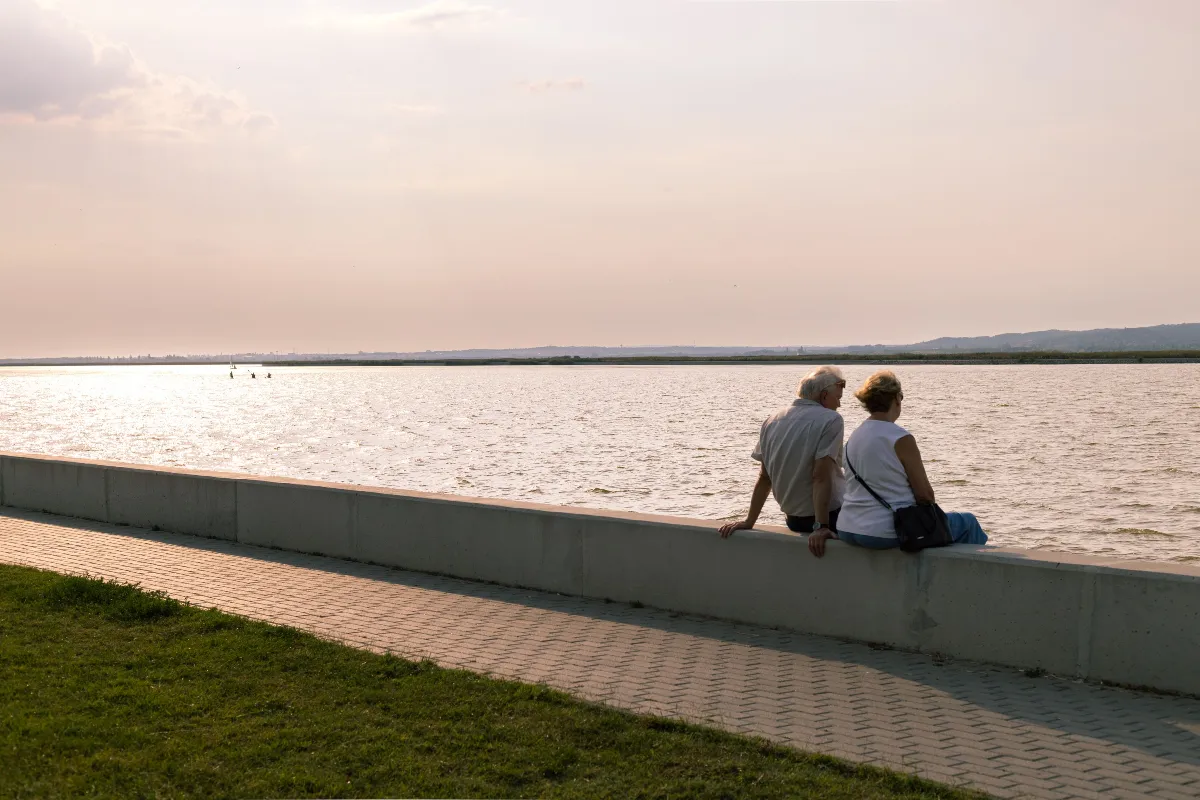 A serene moment of an elderly couple sitting by a lake at sunset, reflecting tranquility. A serene moment of an elderly couple sitting by a lake at sunset, reflecting tranquility.