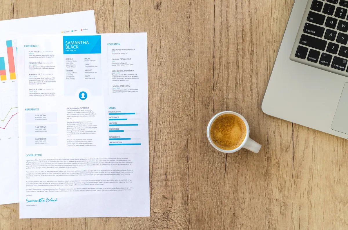 Top view of a desk with resume, coffee cup, and laptop on a wooden surface, ideal for business concepts.